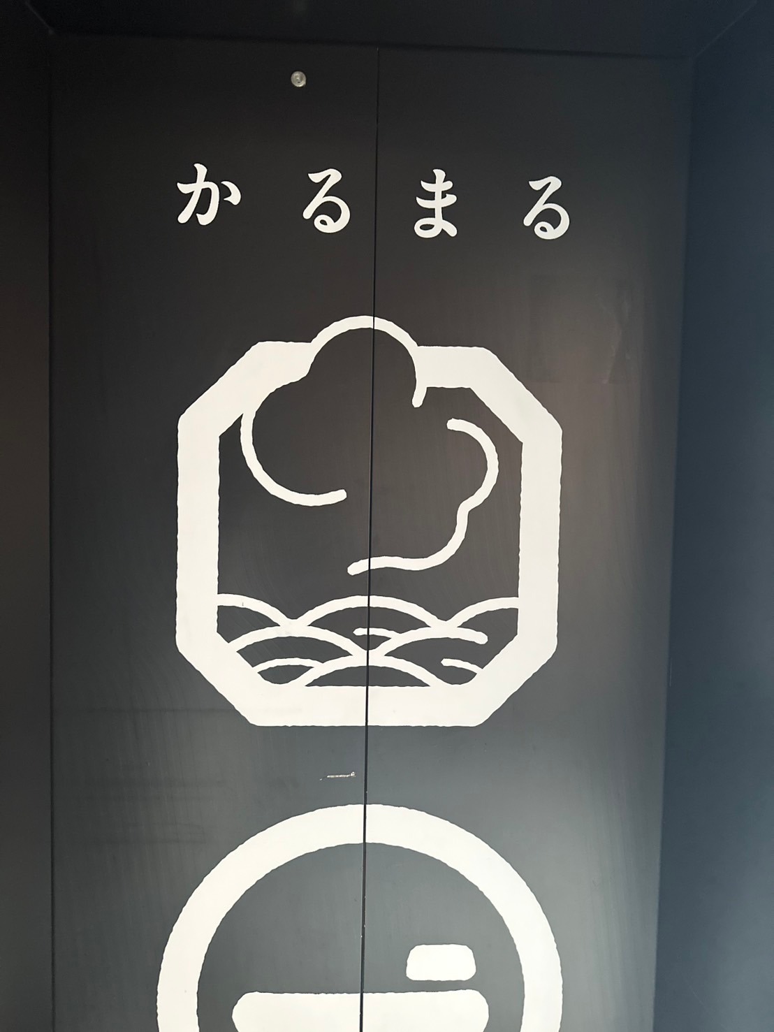 エレベーターの扉に描かれたかるまるの文字とロゴのアップ